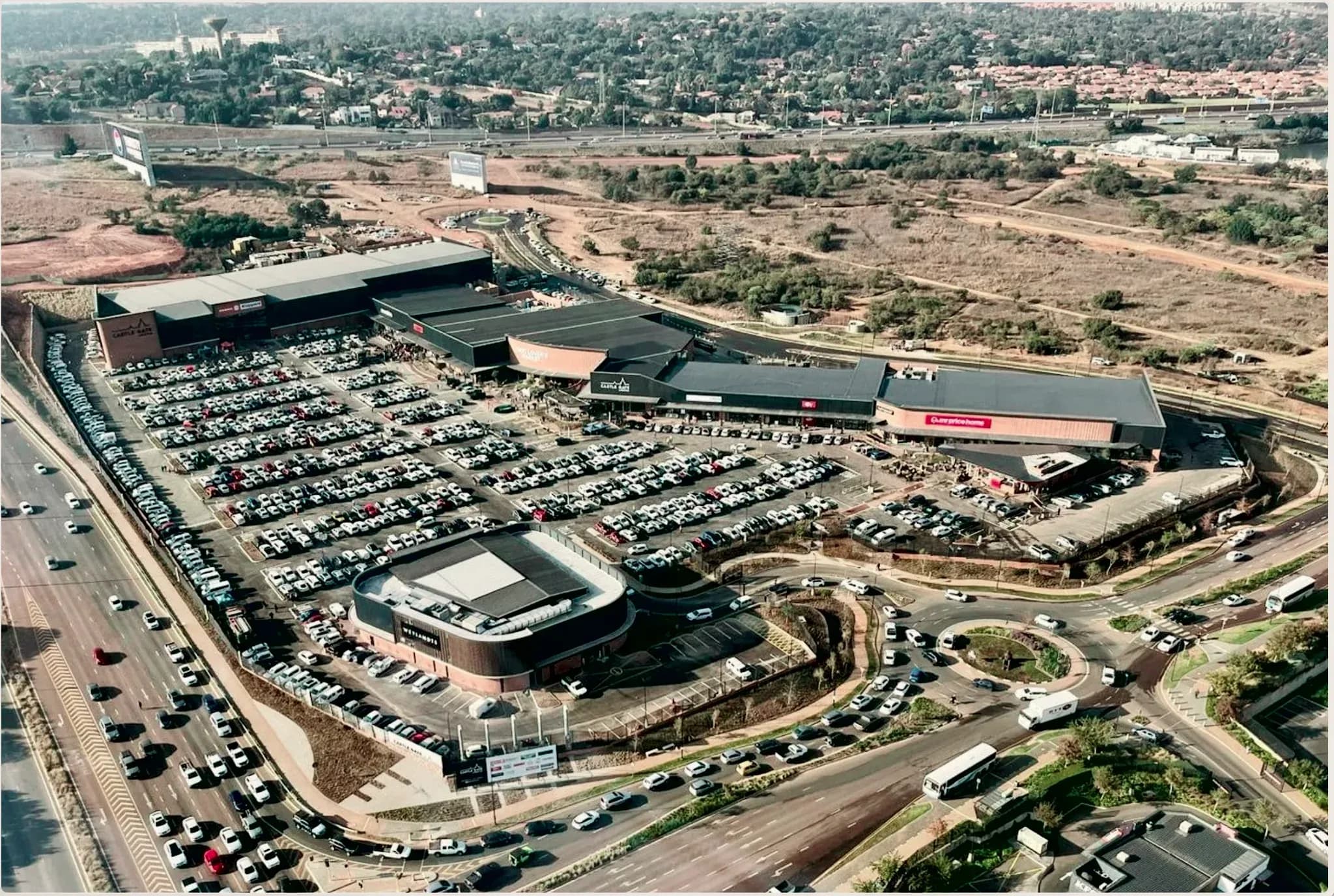 Castle Gate Lifestyle Centre from the air in late afternoon light, the highway running past its parking